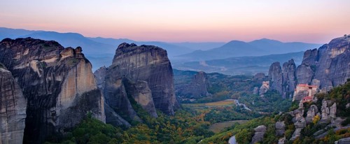 Panoramic view of majestic rock formations and a valley with a monastery at dusk, Meteora valley