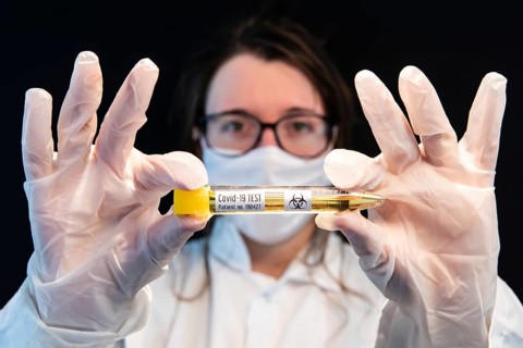 Selective focus shot of vial filled with urine sample and labeled Covid-19 test, held center frame