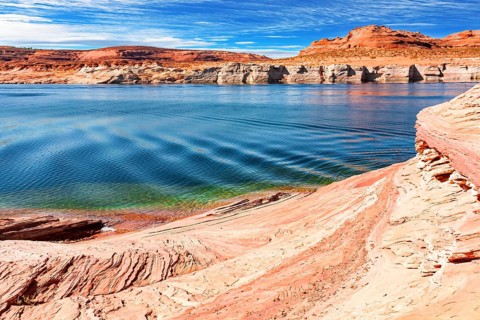 The smooth emerald water of the lake contrasts with the bright red terracotta sandstone shores.