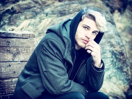 Portrait of young man in hoodie posing outdoor in winter setting with snow all around, looking at
