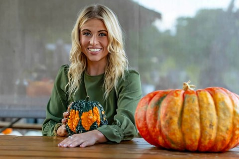 A stunning blonde model poses in a vibrant pumpkin field, wearing a stylish autumn outfit with a