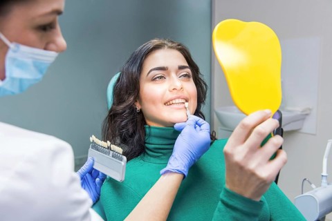 Female dentist, patient holding mirror. Tooth shade chart
