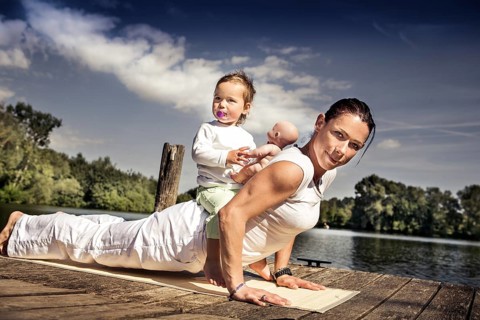 Young woman and her little daughter making yoga exercise at a lake