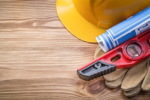 Building helmet protective gloves construction level blueprint on wooden board