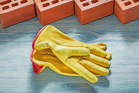 Orange bricks yellow safety gloves on wooden board bricklaying concept