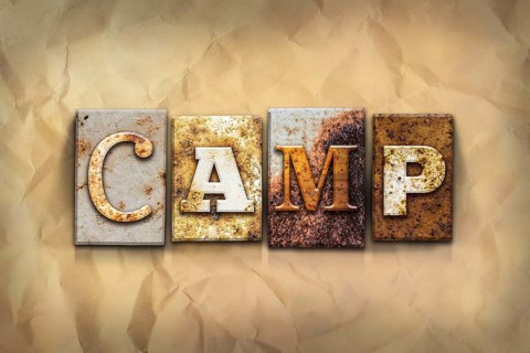 The word CAMP written in rusty metal letterpress type on a crumbled aged paper background