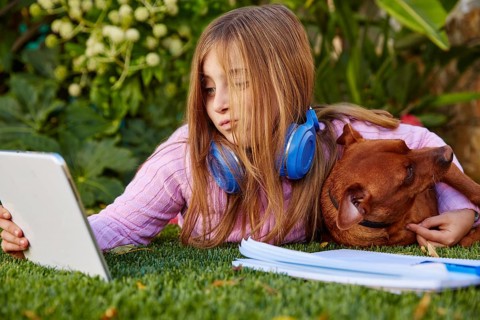Blond kid girl selfie photo with tablet pc and dog lying on grass