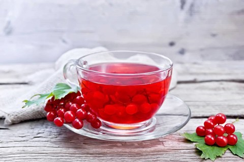 Tea with viburnum in a glass cup, berries and green leaves, burlap on wooden board background