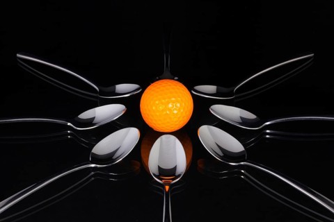 Teaspoons and orange golf ball on the black glass table