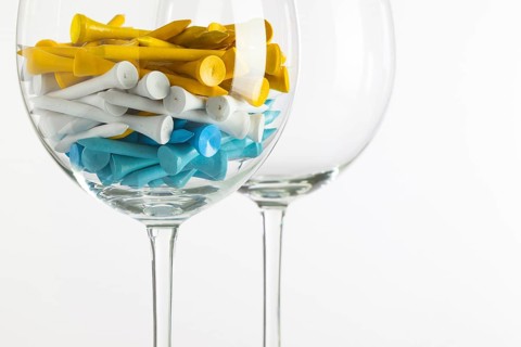 Two glasses of wine and golf equipments on the glass desk