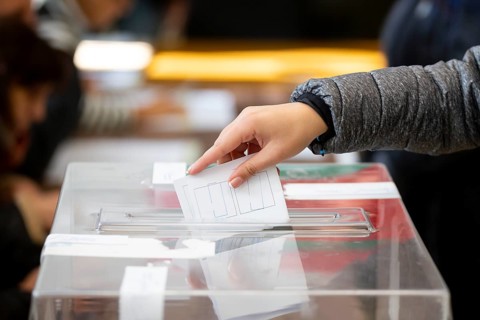 A woman casts her envelope vote into a transparent plastic ballot box. Human hand voting