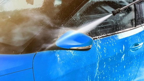 Side mirror of blue car washed in self serve carwash, jet water sprays from high pressure nozzle,