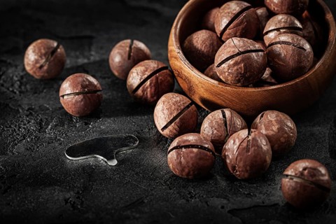 Macadamia Nuts And Key For Open It With Wooden Bowl On Black Background