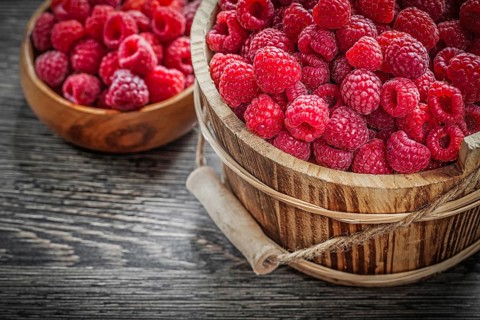 Bowl and bucket with raspberries on wooden board