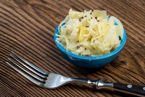 Homemade pickled sauerkraut in a bowl with a fork on a wooden board