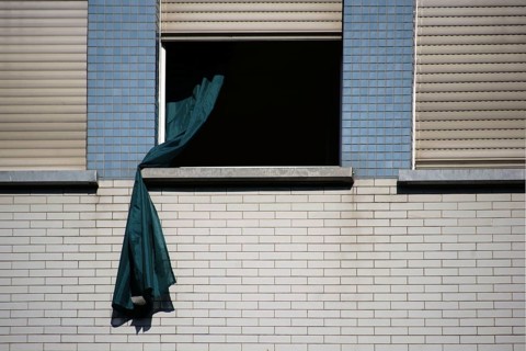 A loose curtain blows out of the window of a brick-built residential building