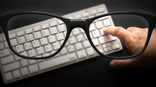 Some black glasses with keyboard sharp and blurred