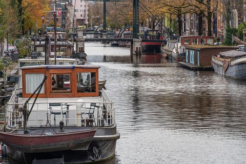 Boats in the city canal, lined with autumnal trees and a bridge, Amsterdam, Netherlands