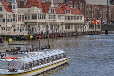 Houseboat in front of a historic building with red roofs on the canal, Amsterdam, Netherlands