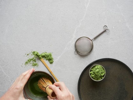 Preparation of green tea drink with matcha powder. Hands with traditional bamboo whisk over bowl of