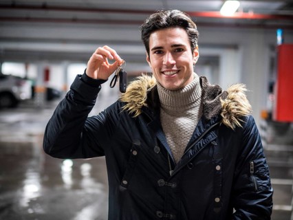 Young trendy man in winter outerwear standing on parking showing alarm remote control to the