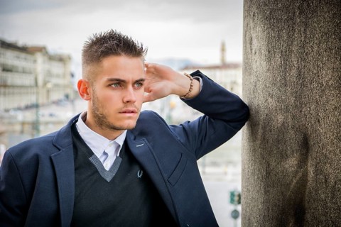 Handsome young man outdoor wearing jacket and shirt standing by historic building in European city.
