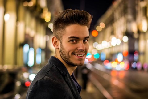 Attractive young man portrait at night with city lights behind him, smiling and looking at camera