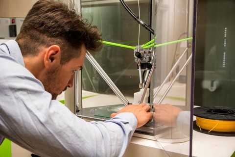 Brunet adult man working with 3D printer, observing the machine at work