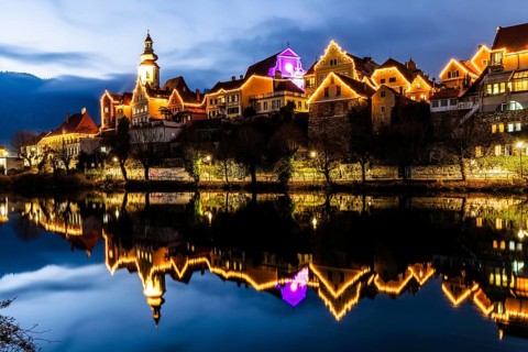Christmas illuminated house facade of Frohnleiten reflected in the river Mur, blue hour,