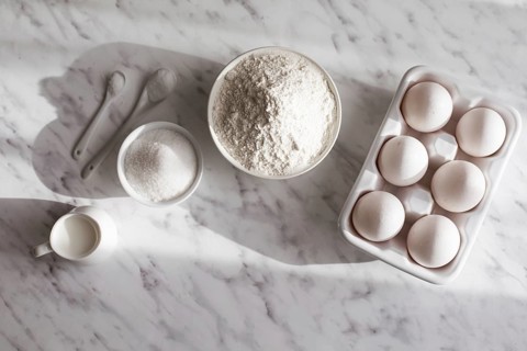 Top view ceramic tray with eggs placed near bowl of flour and sugar. White utensils with white