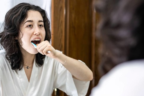 Young woman brushing her teeth in front of the mirror. Happy woman brushing her teeth in the