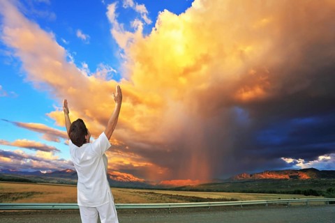 Giant cloud illuminated by the sunset. Yoga on the road. Elderly woman in white performs asana Sun