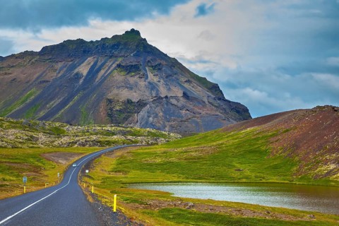 The road passes through the picturesque landscape in the mountains and lakes. Cloud Iceland in the