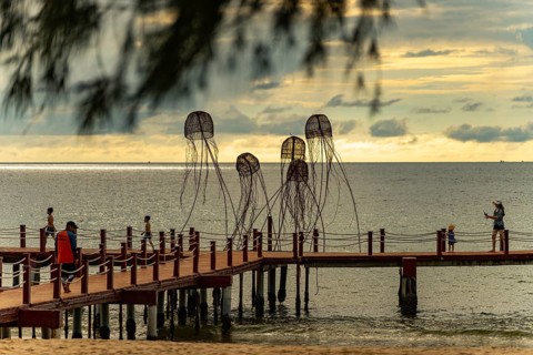 Families walking on a pier with jellyfish sculptures at a peaceful ocean sunset, sun, sunset,