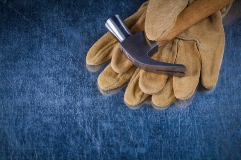 Pair of leather protective gloves with metal claw hammer on scratched metallic background