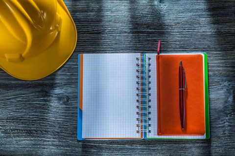 Spiral notepad pen building helmet on wooden board