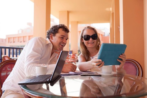 Young couple relaxing over coffee on a balcony sitting at a glass table smiling as they lean close