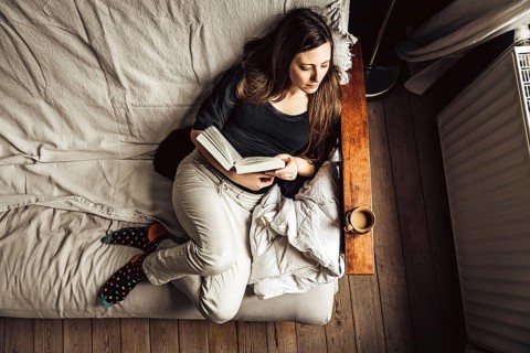 Hig angle view of a 30 yo woman in her sofa, reading a book with a coffee, Brussels