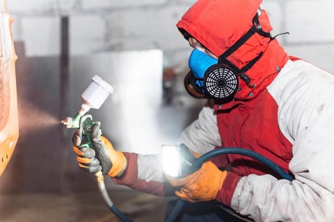 A person in protective gear using a spray gun, illuminating the work area