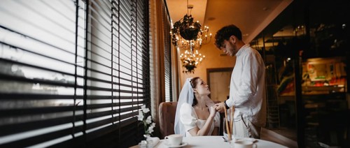 Bride and groom sharing a romantic moment by the window in a softly lit cafe