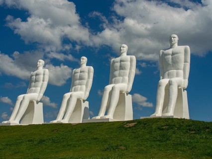Four large white sculptures of seated men on a green meadow under a blue sky with clouds, esbjerg,