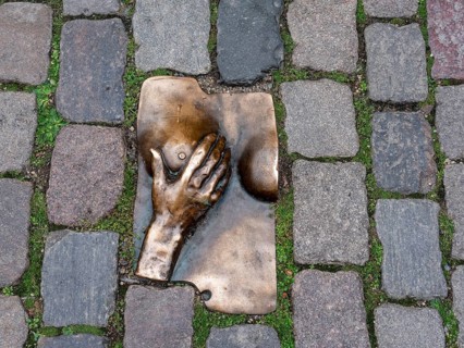 Bronze relief of a hand embracing a female breast on the ground, between granite paving stones in