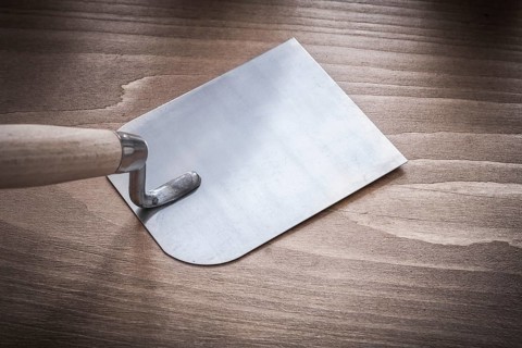 Metal bricklaying trowel on vintage wood board close up view