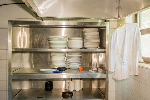 Stacks of dishes on stainless steel storage rack in abandoned resort restaurant kitchen
