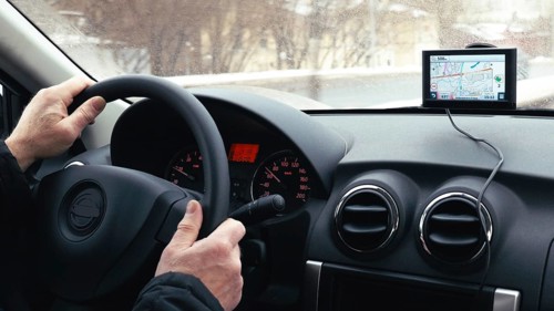 Close-up shot of a man driving a car in winter city. GPS device on the dashboard helps him to find