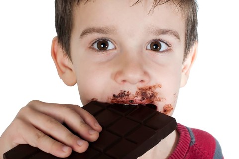 Smiling kid eating chocolate. Smeared stained with chocolate lips. White isolated