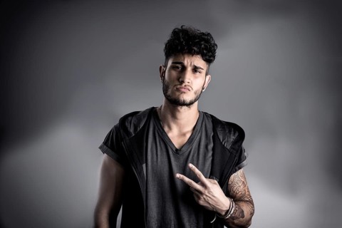 Portrait of handsome young man in dark t-shirt on black background, doing Victory sign with fingers