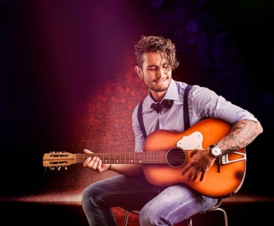 Handsome young man in bow-tie with guitar looking at camera.Studio shot