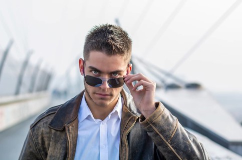Handsome trendy young man standing on a sidewalk, wearing sunglasses and a fashionable leather