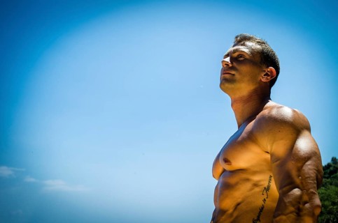 Handsome young muscle man at the seaside, outdoors, showing muscular pecs and torso in front of the